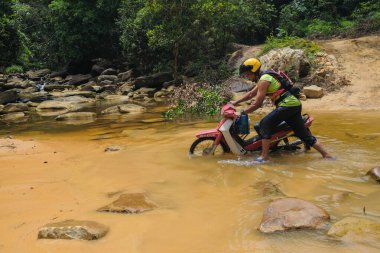 Rompin, Malezya - 11 Ekim 2020: Bir motosikletli bir motosikleti nehirden geçirir. Seyahat ve arkadaşlık kavramı