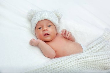 Beyaz bir yatağa sarılıp battaniyeye sarmalanmış sevimli bir bebek. Yeni doğmuş, şapkalı, ponpon şapkalı bir bebek. Yeni doğmuş bir çocuk çerçeveye bakar..