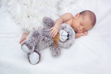 Yeni doğmuş bir bebek uyur büyük bir oyuncak ayıya sarılır