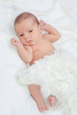 Yeni doğmuş bir bebek pofuduk beyaz bir battaniyenin altında doğrudan kameraya bakar.