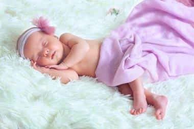 A newborn photo of a little girl sleeping on a soft white fluffy blanket in a pink Tu-Tu skirt and a headband clipart