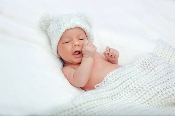 白いベッドにかわいい魅力的な新生児と毛布に包まれた ポンポン付きのニット帽を着た新生児 新生児が目を細めてカメラを見る — ストック写真