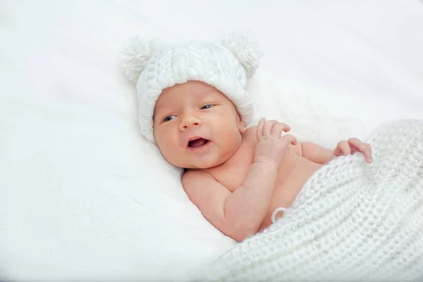 白いベッドにかわいい魅力的な新生児と毛布に包まれた ポンポン付きのニット帽を着た新生児 新生児の少年が横を向いて — ストック写真