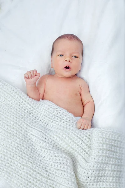 新生児のベッドの上には カメラを見て横になっている 子供は白いニットの毛布で覆われている 子供は注目を集める 口が開いている子供は話すことを学ぶ 最初の音は — ストック写真