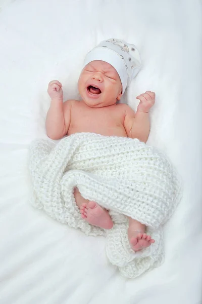 帽子の中で生まれたばかりの少年を泣いている 生まれたばかりの赤ちゃんは疲れていて 白いニットの毛布の下のベッドで空腹です — ストック写真