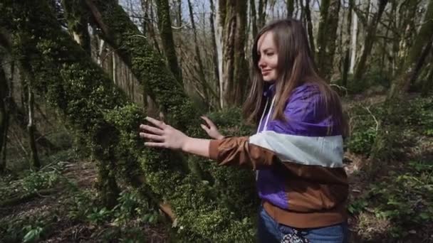 Hermosa chica está acariciando el tronco del árbol que está cubierto de musgo verde grueso — Vídeos de Stock