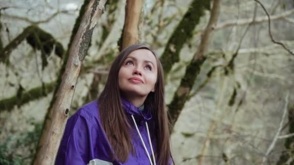 Uma menina doce em uma jaqueta colorida está olhando para as árvores cobertas de musgo na floresta de conto de fadas — Vídeo de Stock