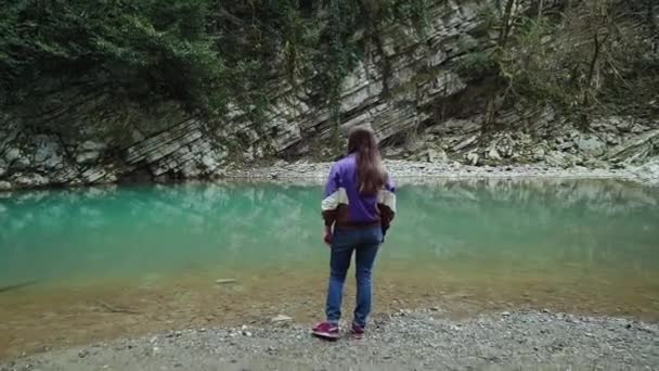 Девушка в непринужденном стиле стоит на берегу чистого голубого озера в горах, масштабируясь — стоковое видео