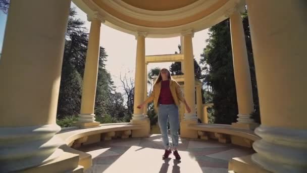 Happy girl whirls in rotunda on a beautiful sunny day, zooming out of the camera. — Stock Video