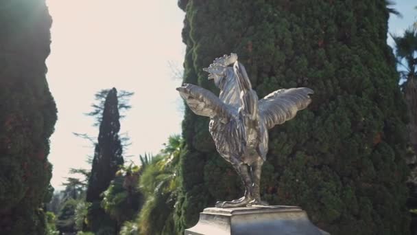 Hermosa estatua de plata de un gallo en un día soleado sobre el fondo de cipreses . — Vídeos de Stock