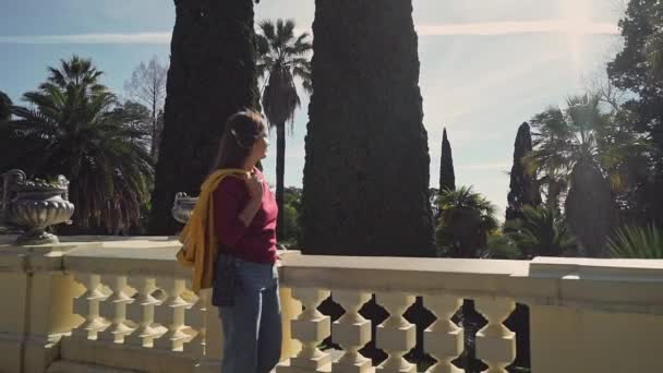 Hermosa chica camina pensativamente en la terraza antigua en el jardín de cipreses a la luz del sol — Vídeos de Stock