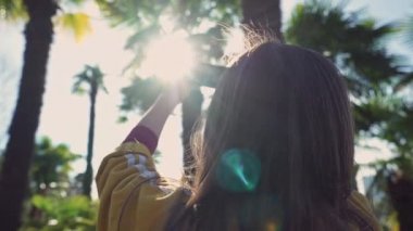 Sarı ceketli kız yakın çekimde güneşli bir günde telefonda palmiye ağaçlarının fotoğraflarını çeker