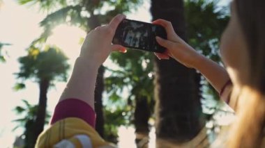 Kız yakın çekimde akıllı telefon palmiye ağaçlarının fotoğraflarını çeker