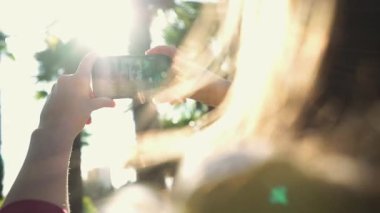 Kız yakın çekimde güneş ışığında palmiye ağaçları akıllı telefon fotoğraflarını çeker