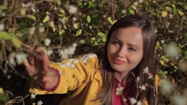 Menina feliz examina flores brancas nos ramos de um arbusto e ela sorri — Vídeo de Stock