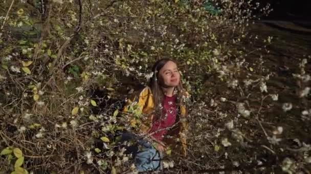 Γλυκό κορίτσι βάζει κάτω από ένα ανθοφορία δέντρο και απολαμβάνει τη μυρωδιά και ηλιοφάνεια — Αρχείο Βίντεο