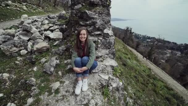 Dolce ragazza è seduta vicino ai resti del muro di una vecchia fortezza su una collina in riva al mare — Video Stock