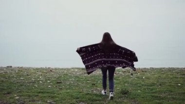 Gelişmekte olan örme bir poncho kız deniz kenarında bir uçurumun kenarında kollarını doğrultma çalışır