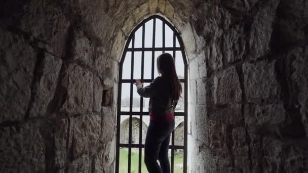 Douce fille se tient debout et regarde par la fenêtre à travers les barres, puis s'assoit pour attendre la libération — Video