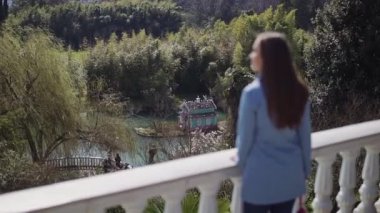 Mavi bir ceket uzun sarı saçlı kız beyaz korkuluk duruyor ve parkta gölet üzerinde kuğu renkli evine bakar