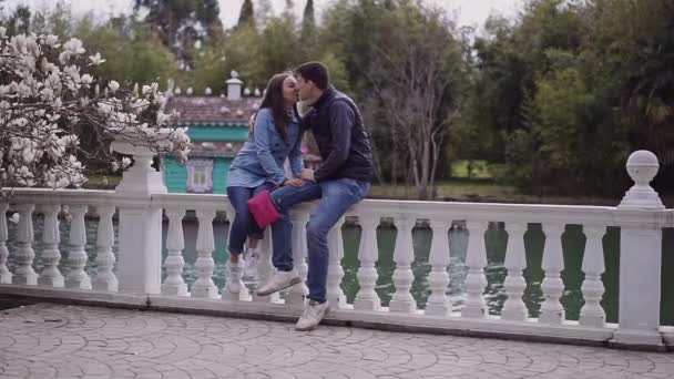 Two lovers is sit in a beautiful flowering garden and kiss each other — Stock Video