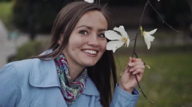Bir gülümseme ile güzel kız manolya beyaz çiçekler inceler ve onları koklar