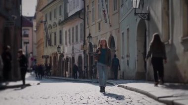 Prag'da akşam güneşinde tarihi binalar ile asfalt sokak boyunca yürüyen rahat giysiler içinde Sevimli kız turist. Ön görünüm