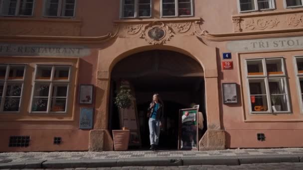 Prag, 15. Mai 2019: Schöne junge Frau kommt aus einem schönen architektonischen Bogen auf eine sonnige Straße. sie setzt ihre Brille auf und geht — Stockvideo