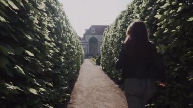 Yeşil park labirentinde akşam güneşinde koşan genç bir kadın. Geri görünüm. Prag'da Wallenstein Bahçesi