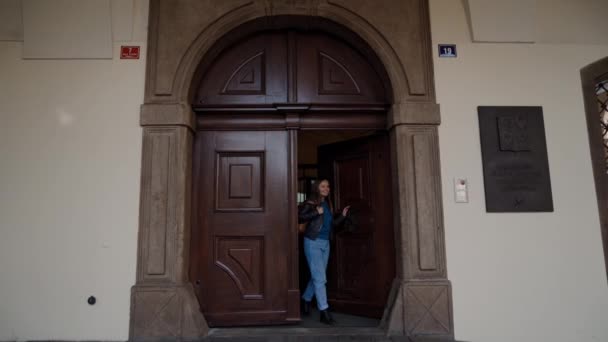 Joven chica feliz en chaqueta de cuero sale de la gran puerta vieja del edificio del parlamento República Checa. Traducción de placa metálica al inglés: Parlamento de la Cámara de Diputados de la República Checa — Vídeo de stock