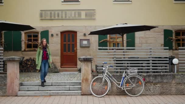 緑のコートを着た美少女がレストランのテラスを出て自転車に乗る。ドイツ。ババリア — ストック動画