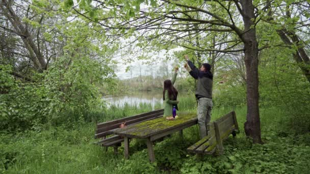 Il tizio con la ragazza sta strappando mele dall'albero a Green Park. Vecchie panche e tavolo in legno ricoperti di muschio verde — Video Stock