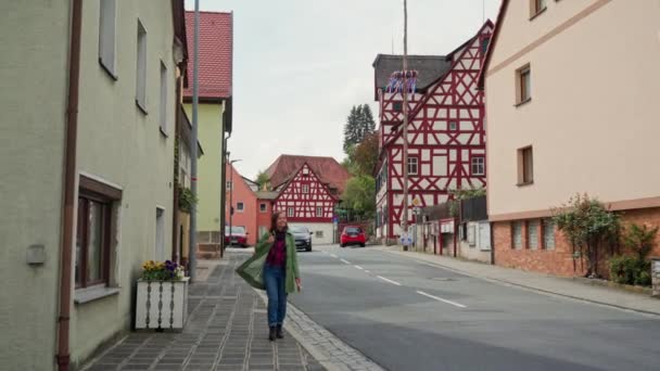 Schöne junge langhaarige Frau in grünem Mantel und Jeans, die in der bayerischen Stadt spazieren geht. glückliches Mädchen genießt Spaziergänge in netter Fachwerkstadt mit alten Häusern in Deutschland — Stockvideo