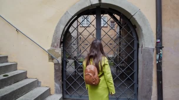 Hermosa joven mujer de pelo largo en abrigo amarillo con mochila que va a dar un paseo en la pequeña ciudad de Alemania. Chica feliz disfrutando de caminar en la pequeña ciudad de madera con casas antiguas en Alemania — Vídeo de stock