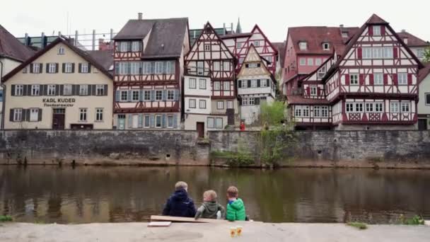 SCHWABISCH HALL, ALLEMAGNE - 5 MAI 2019 : Trois petits garçons amis s'assoient sur le canal et discutent près de l'eau sur fond de maisons traditionnelles à colombages. Schwabisch Hall. L'Allemagne. Plan général — Video