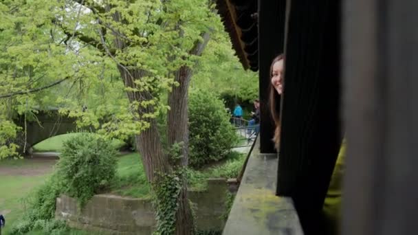 Eine glückliche junge Frau blickt hinter dem Pfeiler der alten Holzbrücke hervor. — Stockvideo