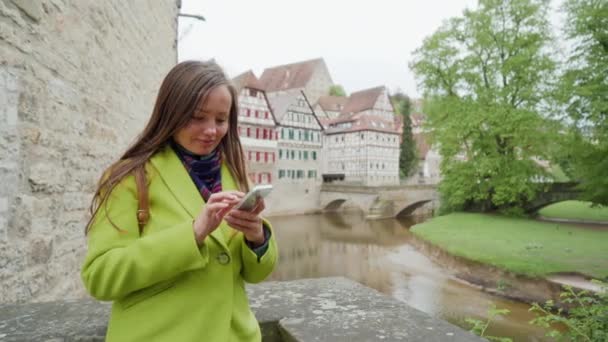 Fiatal nő segítségével okostelefon közelében erőd fal és Sandsteinbrucke híd vagy Steinerner Steg. Favázas építészet. Schwabisch Hall. Németország — Stock videók