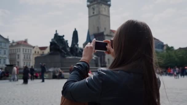 Tourist girl in sunglasses takes picture of sights on the phone in the old square of Prague, Czech Republic — Stock Video