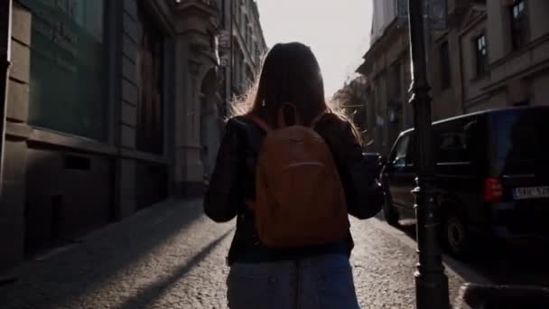 Прага, 15 травня 2019: брюнетка з довгим волоссям і рюкзаком прогулянки по затишних вулицях Старого міста в промені вечірнього сонця, Праги, Чехії. Перегляд назад — стокове відео
