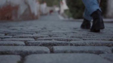 Yakın Avrupa şehirlerinin Arnavut kaldırımlı sokaklarında yürüyen siyah çizme ve kot pantolon bir kadının bacakları