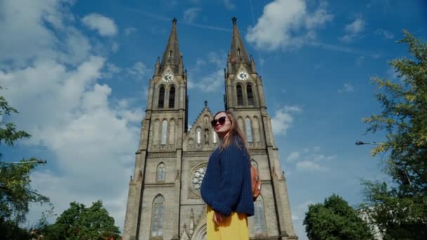 Hermosa chica en gafas de sol se encuentra en el fondo de la iglesia neogótica de St. Ludmila, cámara baja desde atrás, Praga, República Checa — Vídeo de stock