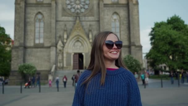 Сладкая длинноволосая девушка в солнцезащитных очках удаляется от великолепной церкви Святой Людмилы в прекрасный солнечный день, портрет, Прага, Чехия — стоковое видео