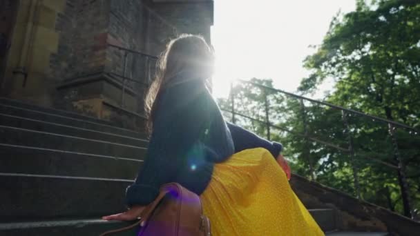 Chica feliz en ropa colorida se sienta en los pasos del templo, rayo de sol juega en su pelo largo, abajo bajo — Vídeos de Stock