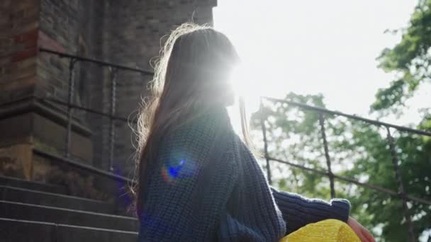 Menina em óculos de sol senta-se em degraus de pedra no sol e ela sorri, retrato — Vídeo de Stock