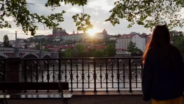 Prachtig uitzicht vanaf de dijk van de rivier de Moldau bij zonsondergang in daken van huizen. Lief meisje komt tot hek om te kijken naar dit schilderachtige uitzicht, Praag, Tsjechische Republiek — Stockvideo