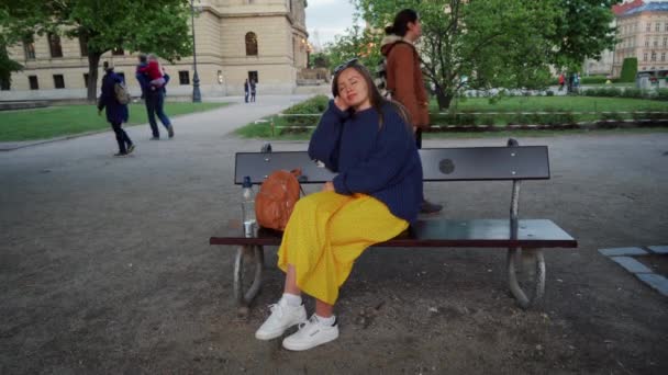 Praag, 1 mei 2019: mooi meisje in lange gele rok zit op bankje in Park en ze buigt soms haar ogen — Stockvideo