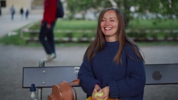 Süßes Mädchen sitzt im Park und spielt mit grünem Apfel: wirft sich hin, verschränkt die Arme, lächelt — Stockvideo