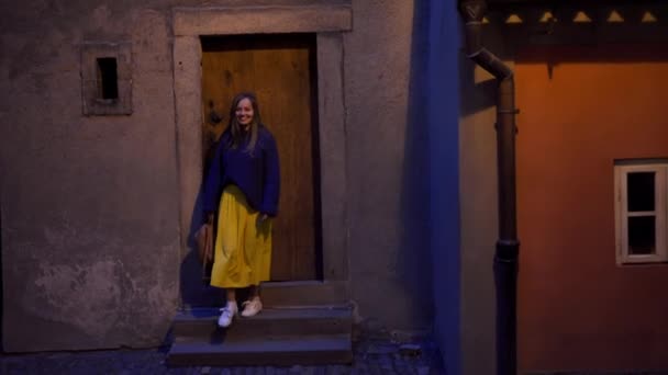 Fille souriante avec sac à dos dans ses mains descend les escaliers dans des lanternes lumière chaude dans l'heure du soir — Video