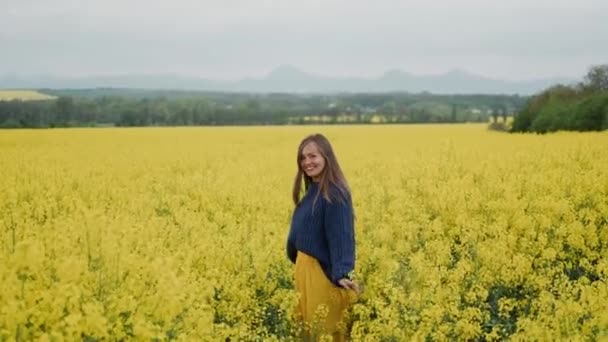 Hermosa mujer de pie en un campo de flores amarillas con los brazos extendidos — Vídeos de Stock
