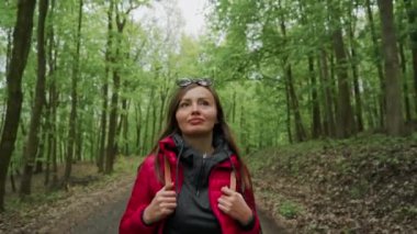 Orman yolu boyunca aktif sağlıklı kadın yürüyüş. Kırmızı ceket ve güneş gözlüğü güzel kadın turist portresi. Rekreasyon, güzel manzara, spor, seyahat